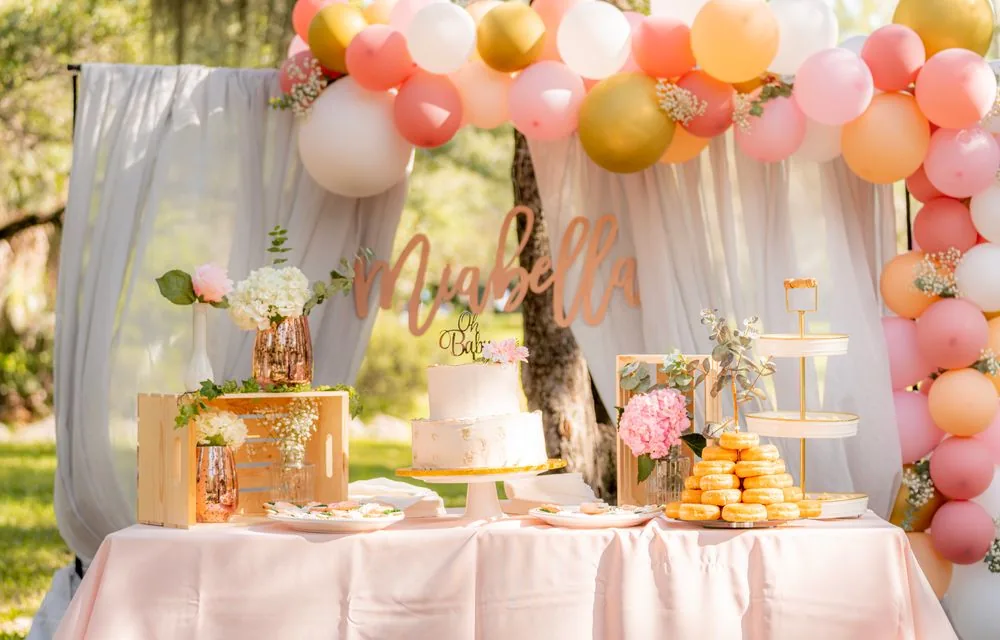 An elegant baby shower table with a balloon arch and greenery
