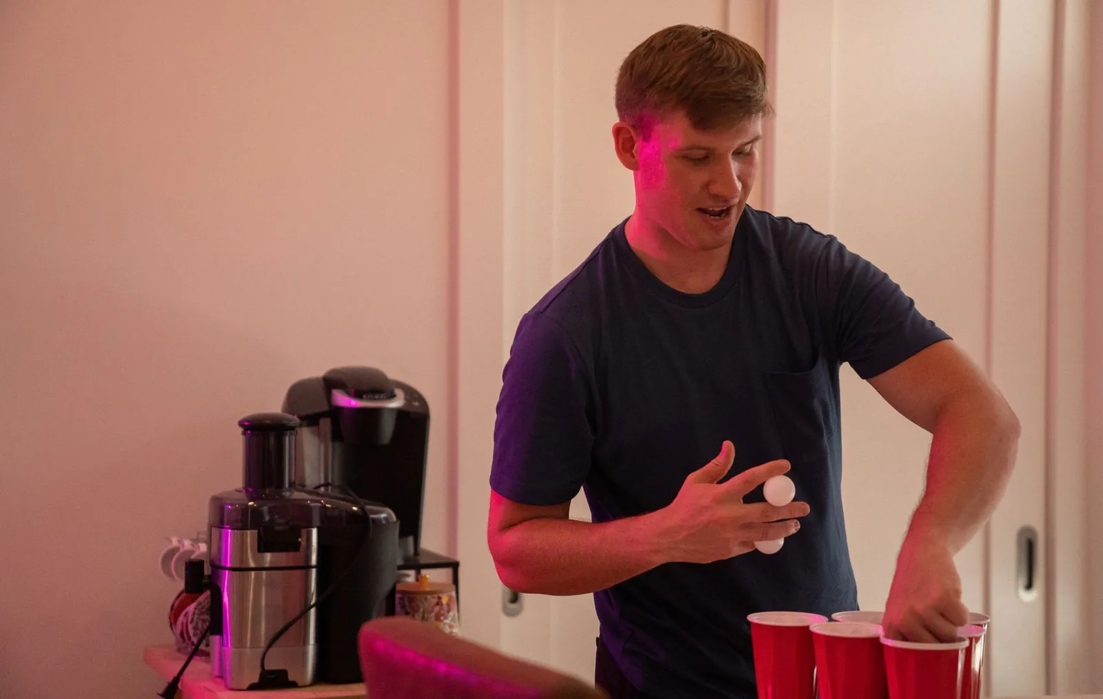 Guest tossing a ping pong ball into a row of cups at a party, the setup used for diaper pong