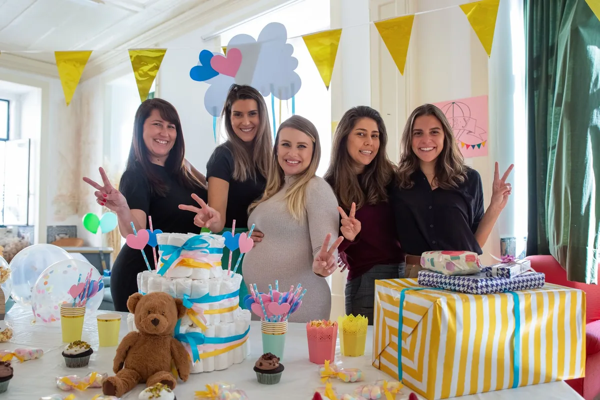 Friends at a baby shower next to a diaper cake and gifts, ready for the diaper raffle